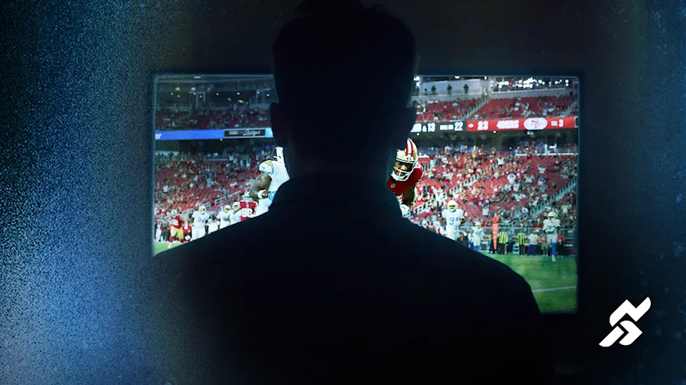 Silhouette of a person watching a football game on a television screen